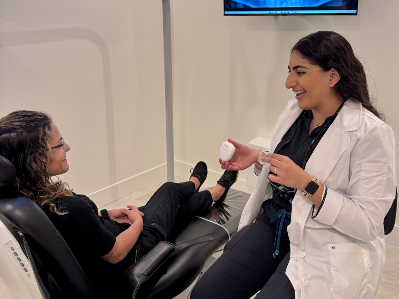 Dentist and dental assistant wearing masks consult with patient holding mirror during a checkup in a treatment room - Maitland Dentist