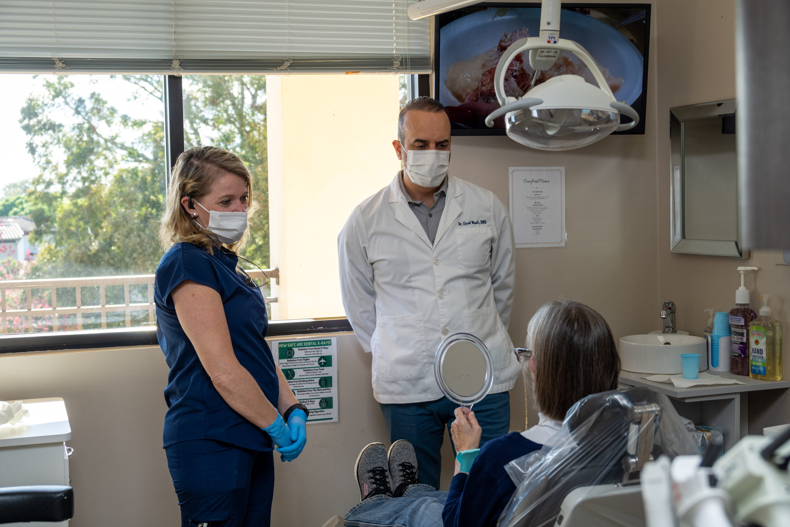 Dr. Maali and an assistant with a patient who is appreciating their new smile - Dentist Orlando Dr. Maali and an assistant with a patient who is appreciating their new smile - Dentist Orlando